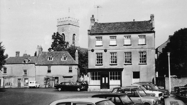 The Market Square in Stony Stratford looking to east side of Square old cottages with old van parked in front of the church tower behind large house to the left. Photo taken in 1971
