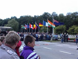 Colour photograph showing onlookers watching a parade approaching the Ploegsteert Memorial to the Missing at the Royal Berkshire Cemetery Extension.
