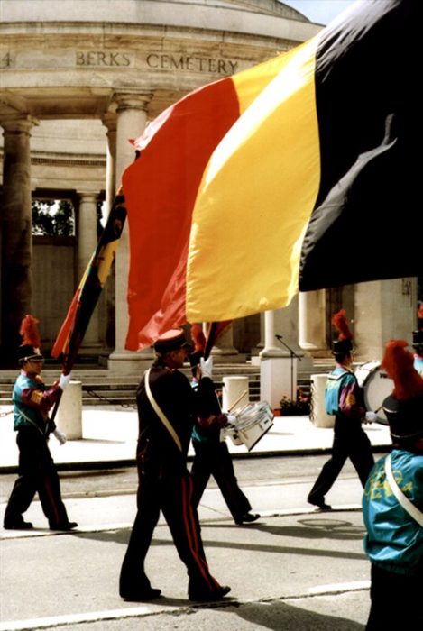 Colour photograph showing part of a parade band marching past the Ploegsteert Memorial to the Missing at the Royal Berkshire Cemetery Extension.