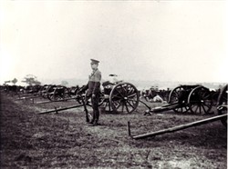 Photograph of a soldier stood with a line of gun carriages.