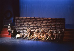 Slide of 7 soldiers sat or lying on the floor in front of a 'wall' with one sat on steps to the side