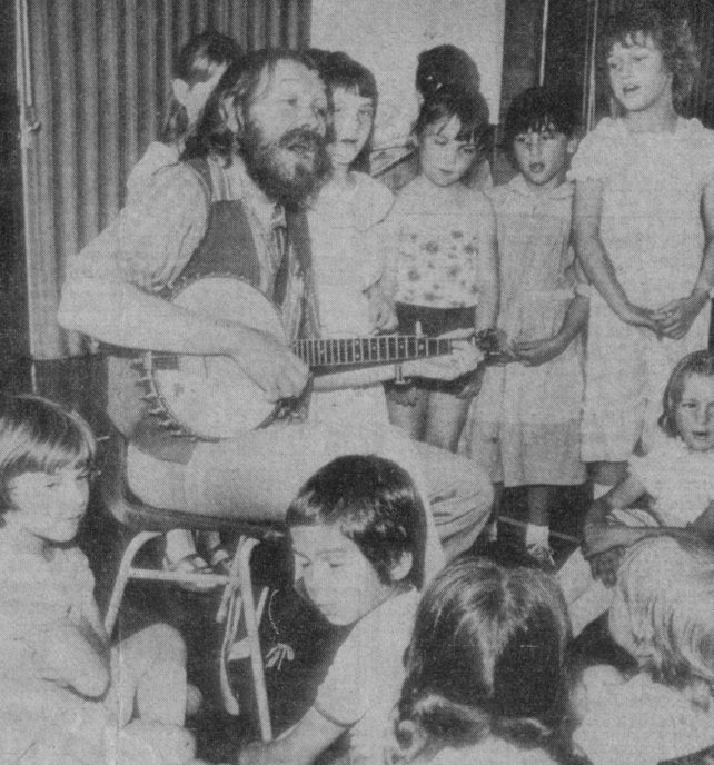 John Roberts with his guitar and a group of children