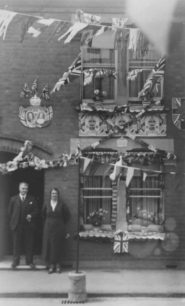 Couple standing in front of large house decorated  for a Coronation.