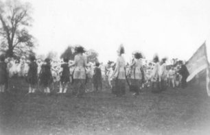 Groups of children and women in fancy dress in a field.