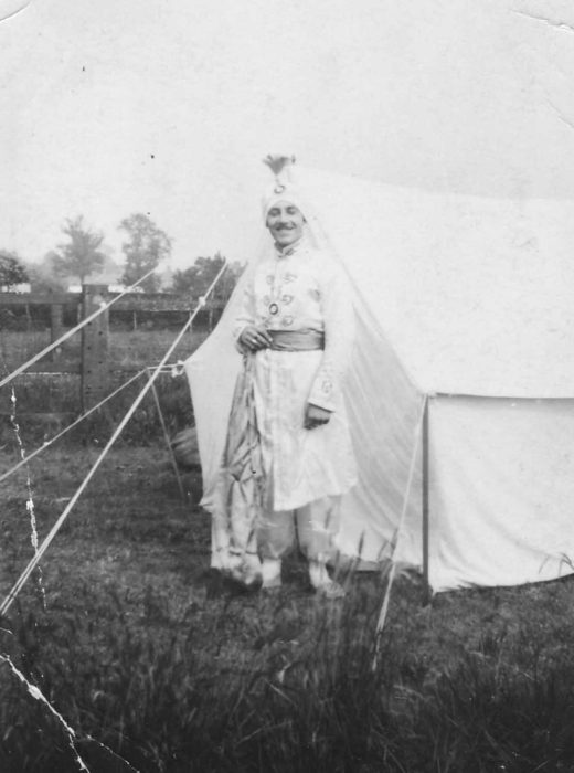 Man in Indian costume standing by a tent