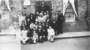 Group of adults and children posing in front of a decorated house.