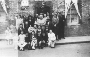 Group of adults and children posing in front of a decorated house.