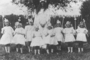 Group of eight girls and a woman in a field, in fancy dress.