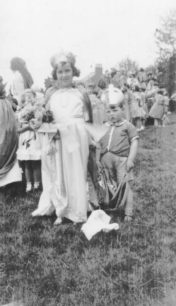 A young carnival queen with a reluctant pageboy, in a field