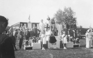 Parade group on a podium in a field featuring Britannia along with airmen, soldiers, sailors, doctors and nurses