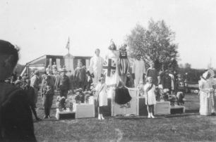 Parade group on a podium in a field featuring Britannia along with airmen, soldiers, sailors, doctors and nurses