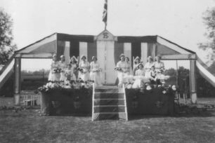 A group of women in white dresses and with bouquets, on a stage in a field