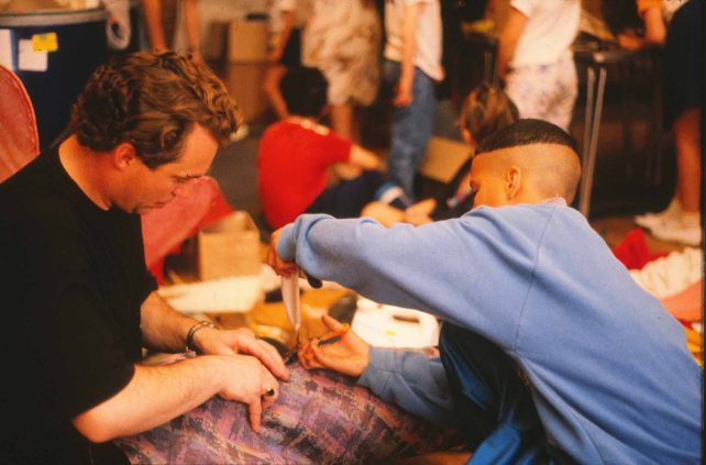 A man helping a boy while he cuts some fabric