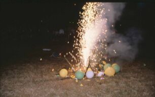 A roman candle goes off surrounded by balloons