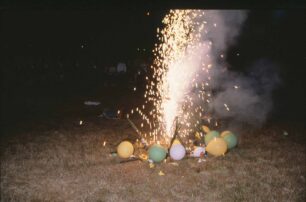 A roman candle goes off surrounded by balloons