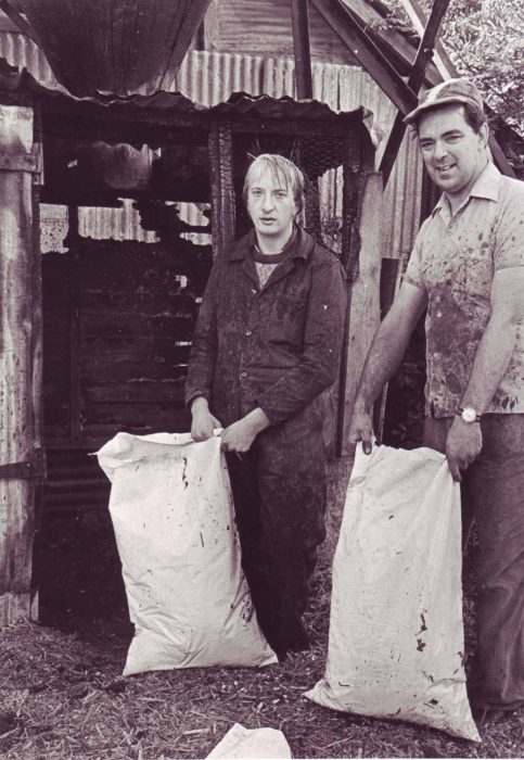 Two men with sacks in front of a fire damaged shed